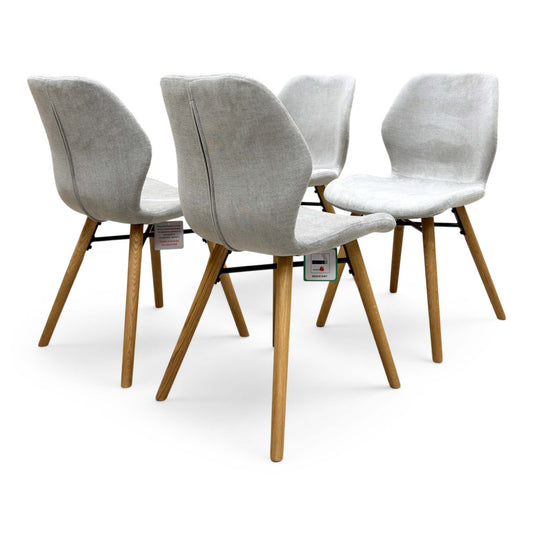 Full view of the A set of four Furniture Village ‘Stockholm’ upholstered dining chairs featuring a continuous curved back and seat design with dark solid oak legs.