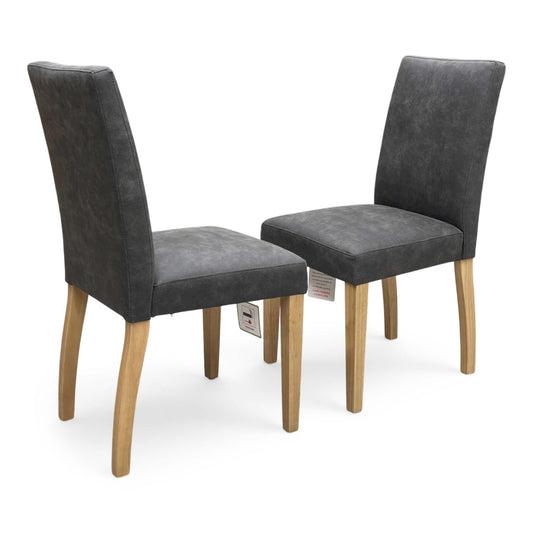 Full view of a pair of Furnitureland ‘Augusta’ Dining Chairs in Grey Cowboy fabric, showcasing their contemporary diamond-stitched quilted backs, supportive scoop silhouettes, and sleek black metal legs.