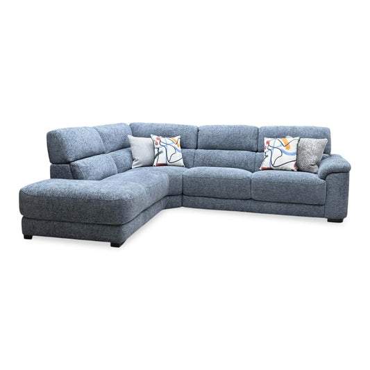 Full view of the Nova corner chaise end sofa in silverish blue fabric, showcasing its spacious L-shaped layout, contemporary block-cushion design, and plush scatter cushions.