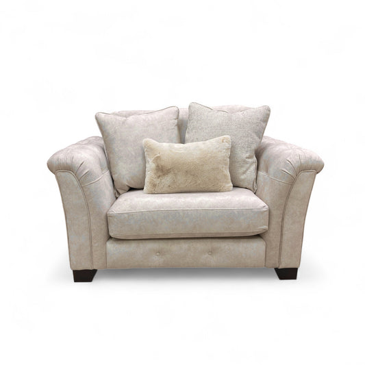 Beige fabric snuggler armchair with rolled arms and accent pillows.