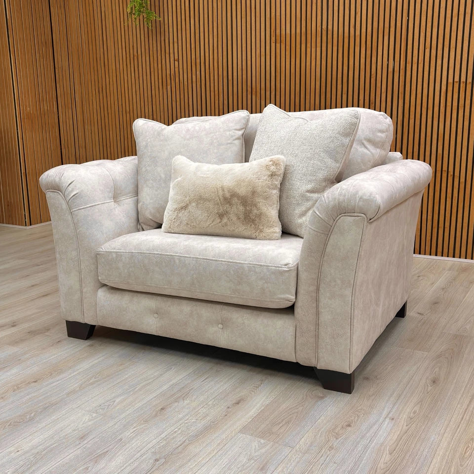 Beige fabric snuggler armchair with rolled arms and accent pillows.