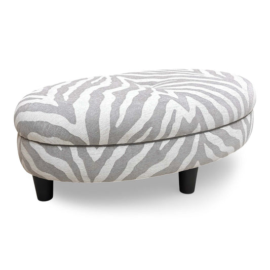 Full front-on view of the 'Zanzibar' oval footstool, showcasing the bold black and white zebra pattern fabric.