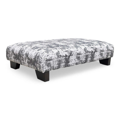 The ‘Aura’ Kai Grey Designer Footstool upholstered in soft chenille fabric, featuring a modern low-profile design and dark wood feet.
