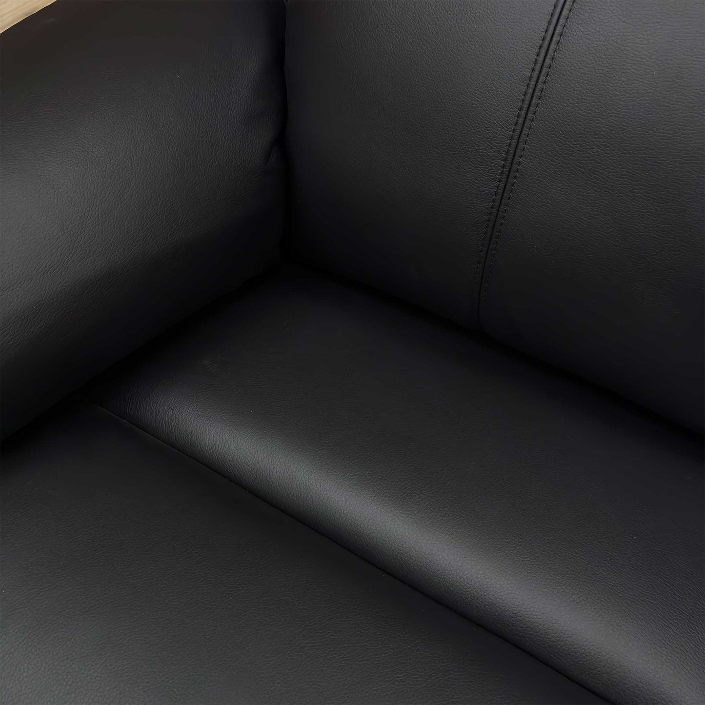 Close-up of the 100% top-grain black leather upholstery, showing the natural grain texture and precise perimeter stitching.