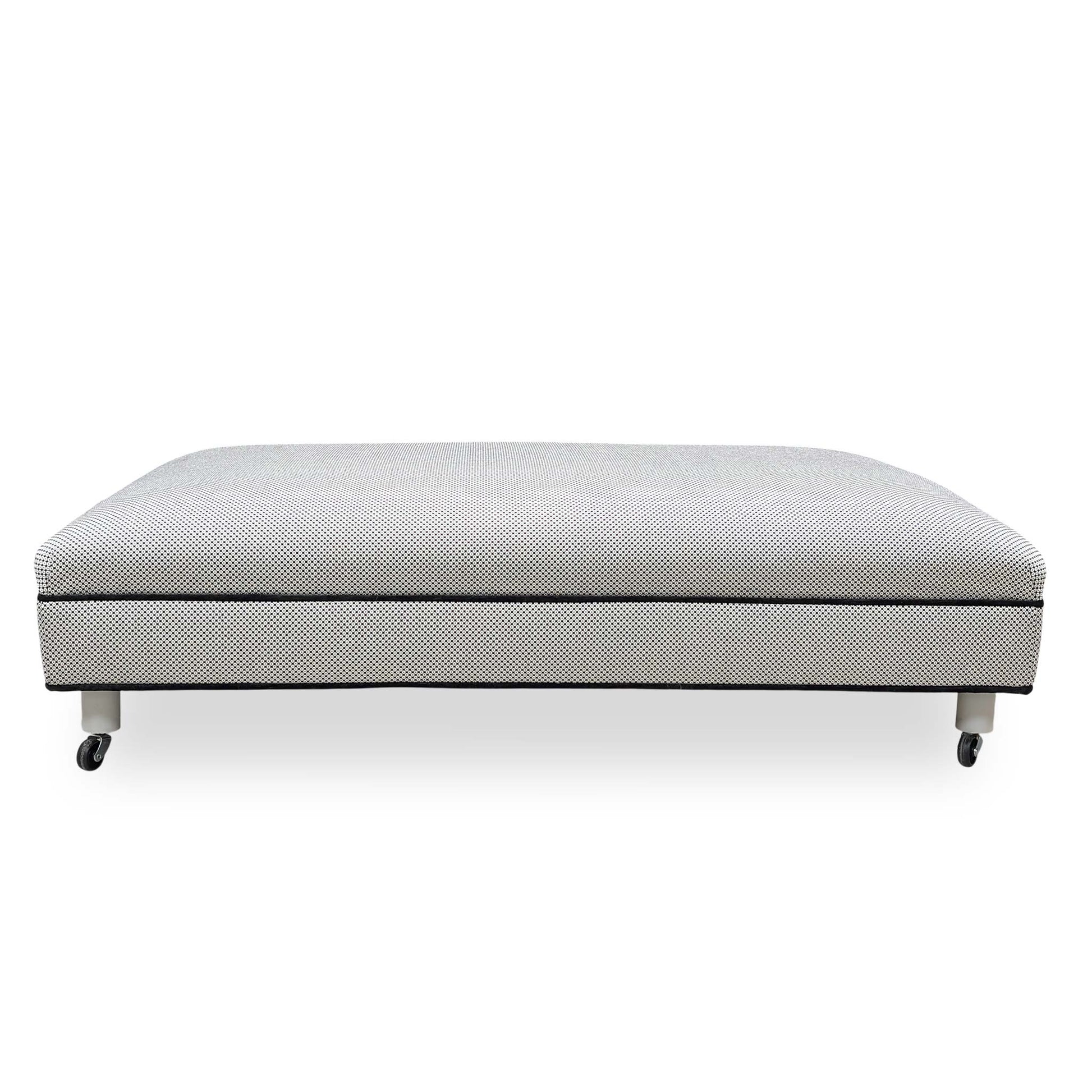 Side profile of the Ambassador footstool showing the uniform upholstered base and sleek contemporary silhouette.