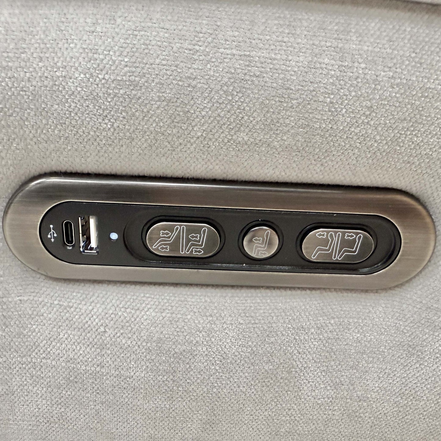 Close-up of the integrated chrome power controls on the side for recliner and headrest adjustment.