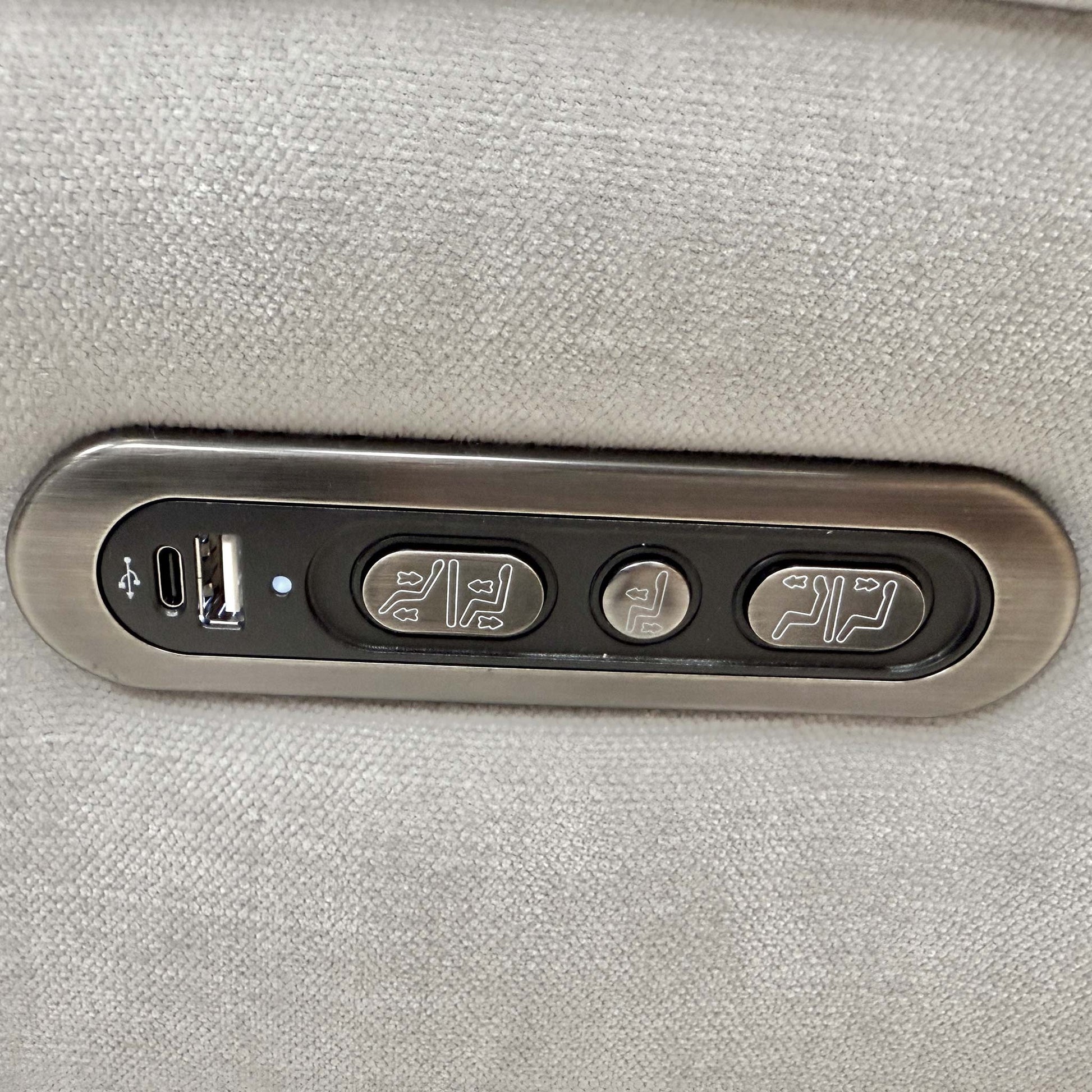 Close-up of the integrated chrome power controls on the side for recliner and headrest adjustment.