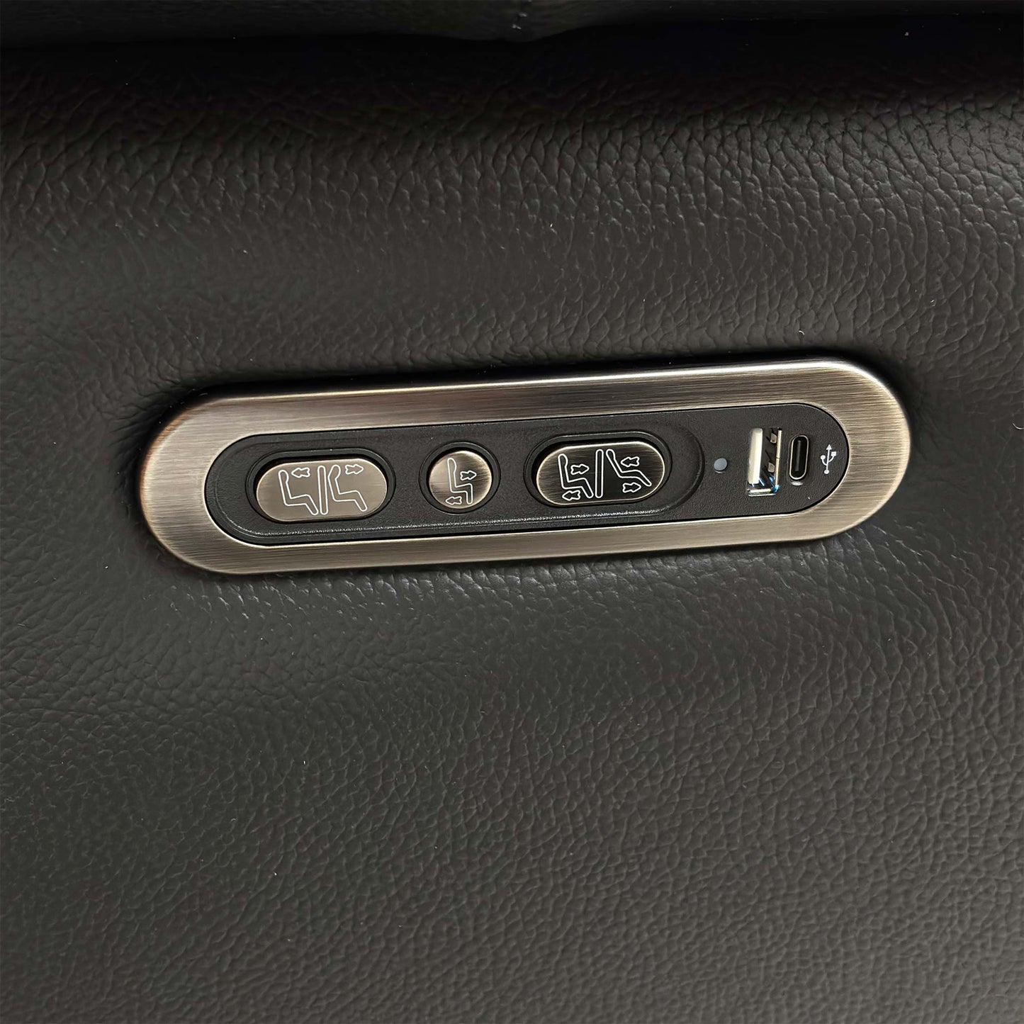 Close-up of the integrated metallic power reclining controls located on the side of the black leather armchair.