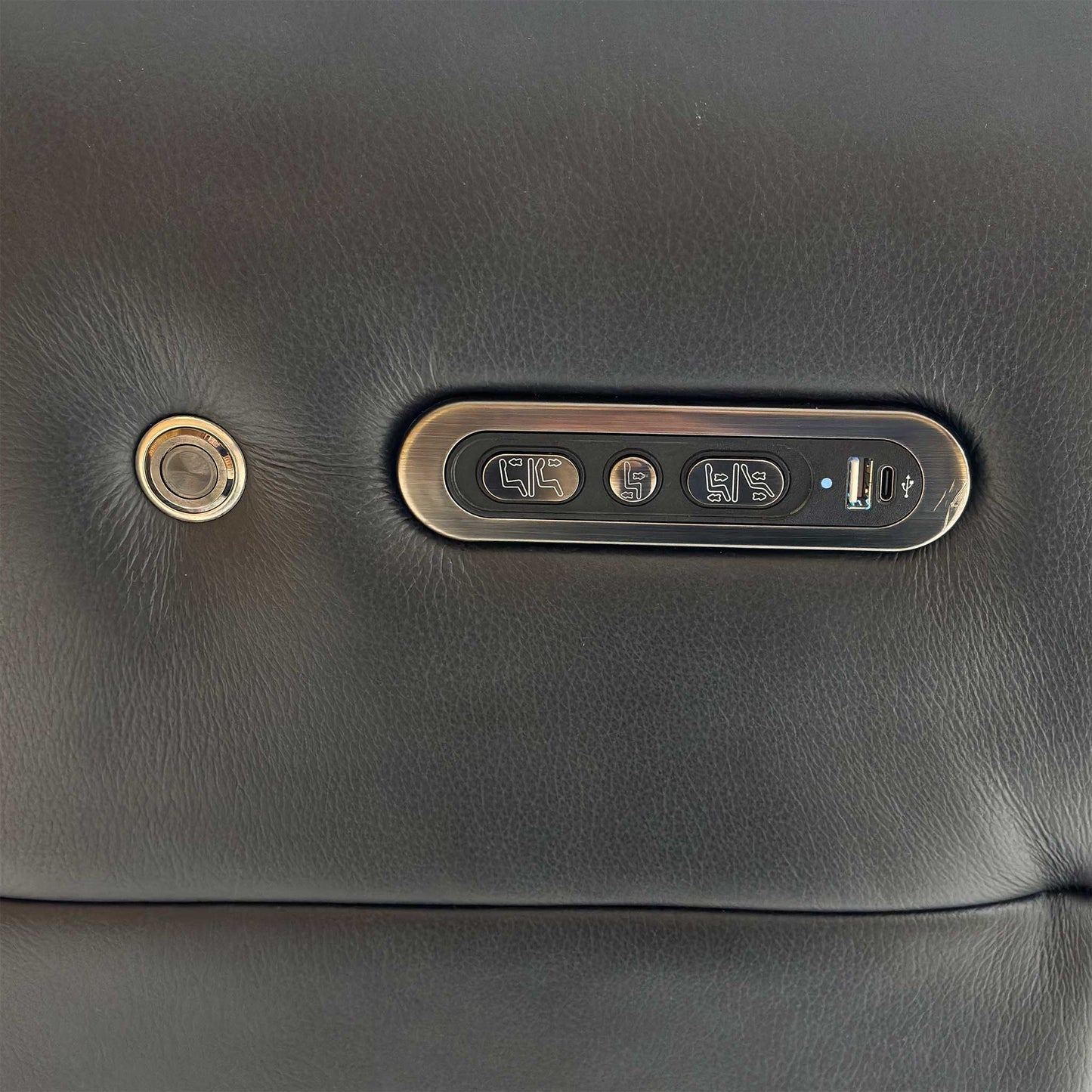 Close-up of the side-mounted power controls on the jet black leather sofa, featuring buttons for reclining, headrest adjustment, and a built-in USB charging port.
