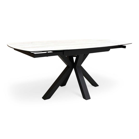 Full view of furniture Village ‘Raul’ 120cm swivel extending dining table featuring a travertine-effect ceramic top and a black starburst metal base.