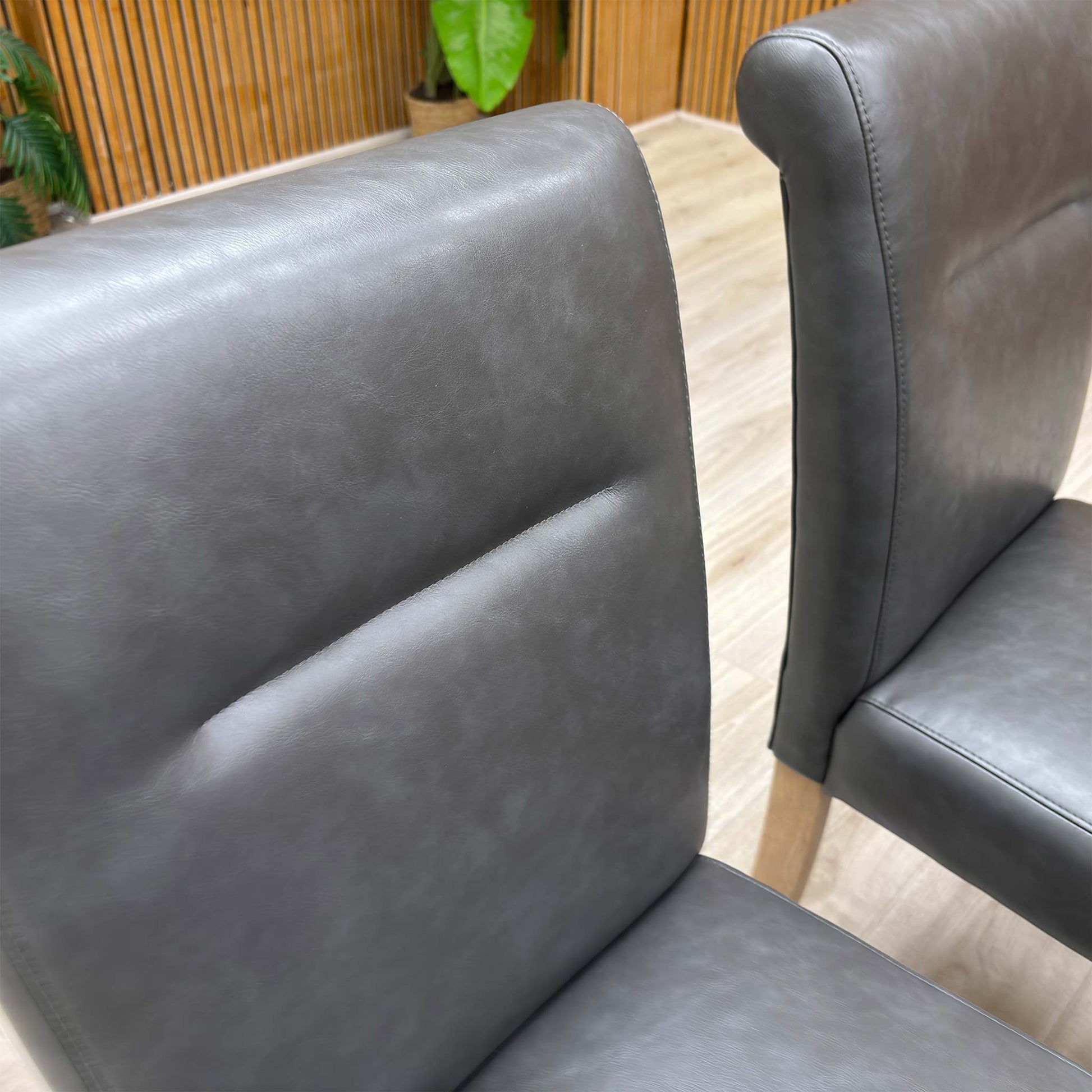 Close-up of a dark grey roll-back chair in a home setting, highlighting the sophisticated faux leather texture.