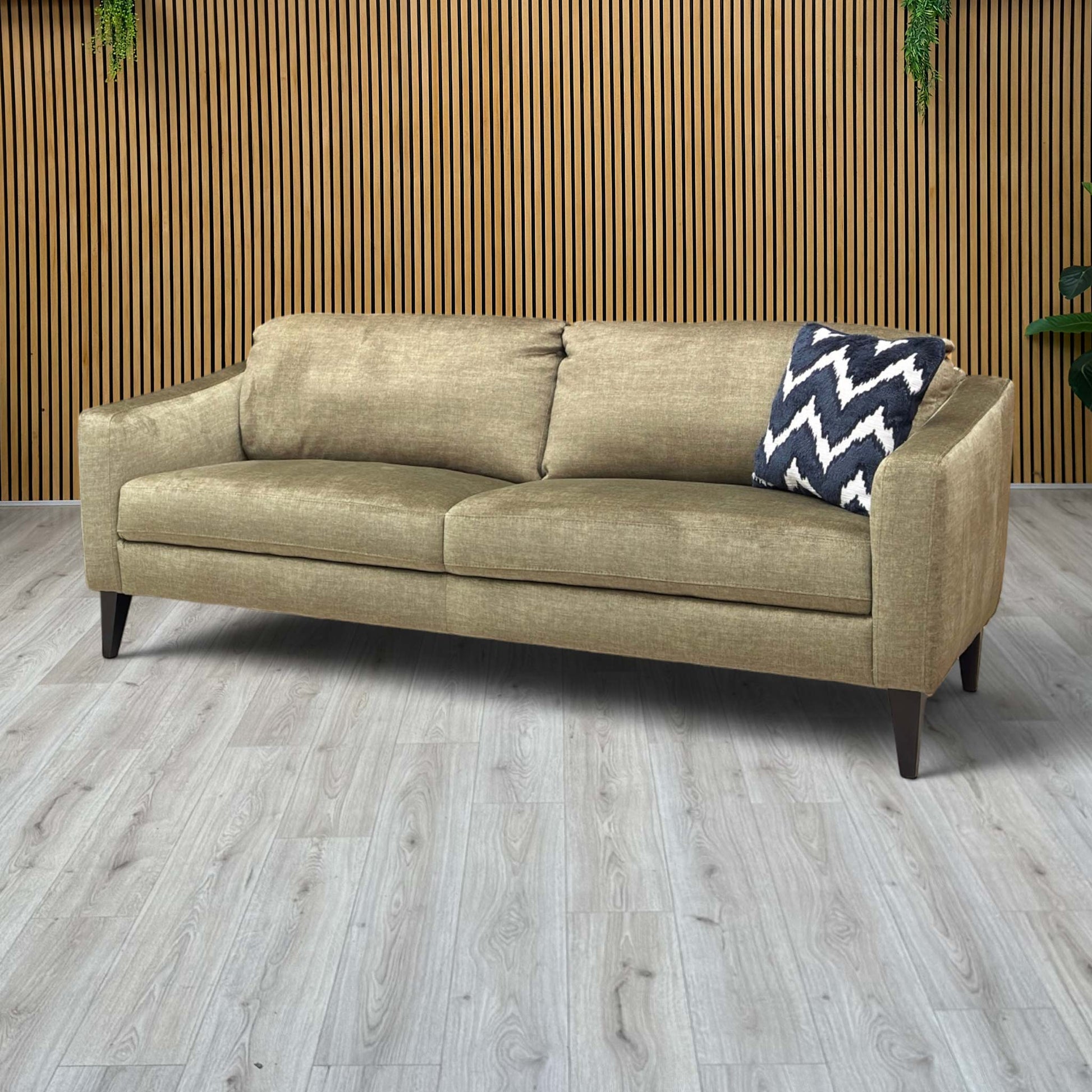 Lifestyle view of the Oslo sofa in Vogue Olive, showcasing the deep seat cushions and the elegant contrast between the green velvet and the slim dark legs.