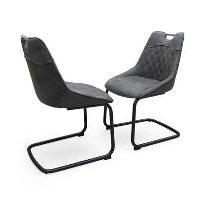 Full view of a pair of ‘Warrior’ Cantilever Dining Chairs in Charcoal Grey fabric, showcasing their sleek contemporary C-shaped frames, vertical channel-stitched backs, and minimalist industrial profile.