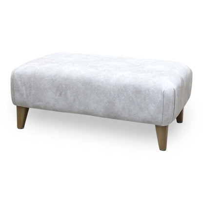 Side profile view demonstrating the footstool's compact height, balanced linear proportions, and tightly upholstered base paneling.