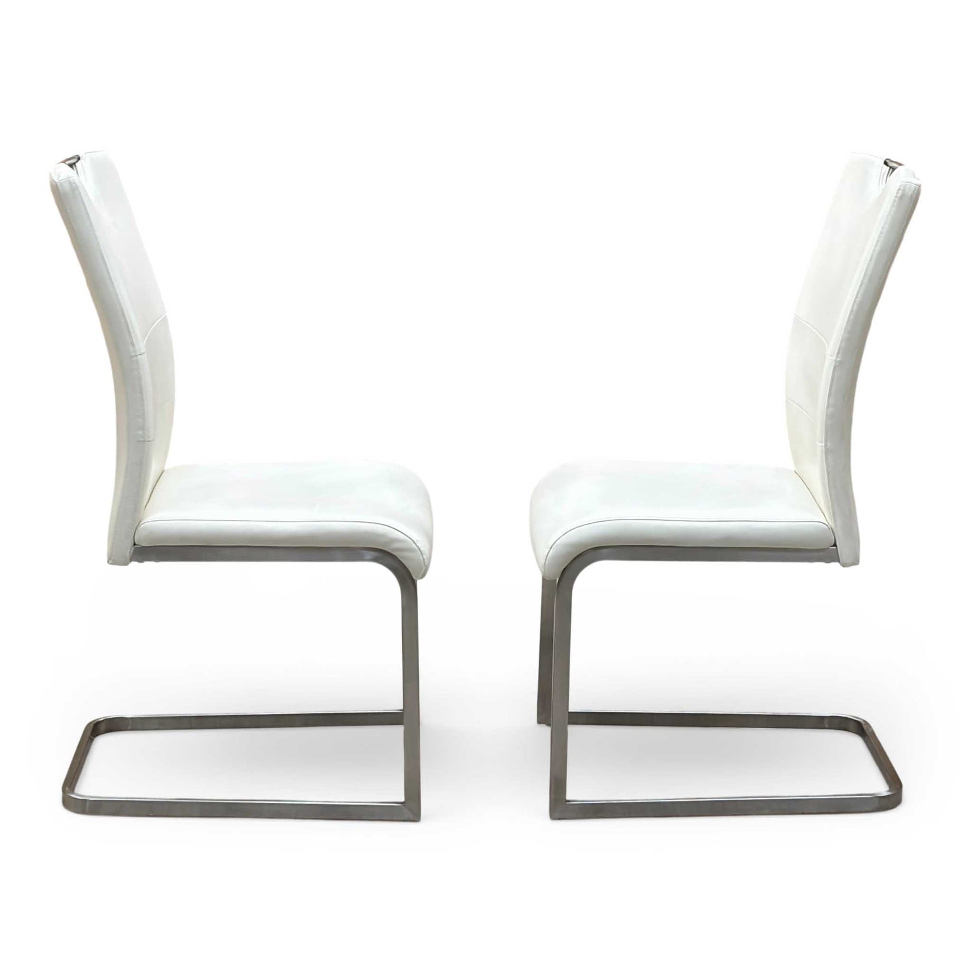 Front-facing view of the two Bianco white faux leather dining chairs arranged side-by-side, highlighting their clean vertical stitching patterns, contoured padded seats, and elegant symmetry.