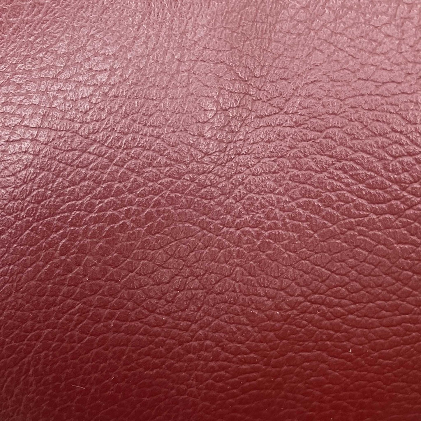 High-definition close-up macro view of the premium Burgundy Red pure leather, detailing the natural fine pebble grain texture, soft supple surface finish, and deep, rich wine-red tonal depth.