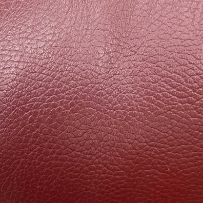 High-definition close-up macro view of the premium Burgundy Red pure leather, detailing the natural fine pebble grain texture, soft supple surface finish, and deep, rich wine-red tonal depth.