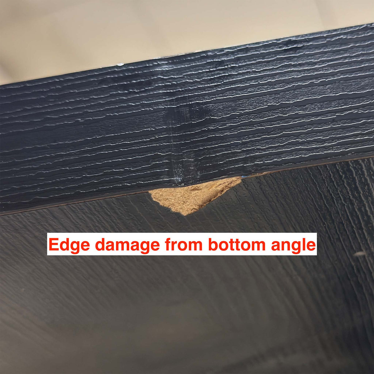 Close-up from below of a chip on the edge of the Magda black oak table exposing the pale core