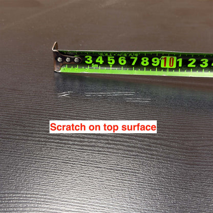 Close-up of a fine scratch on the top surface of the Magda black oak table, tape measure for scale