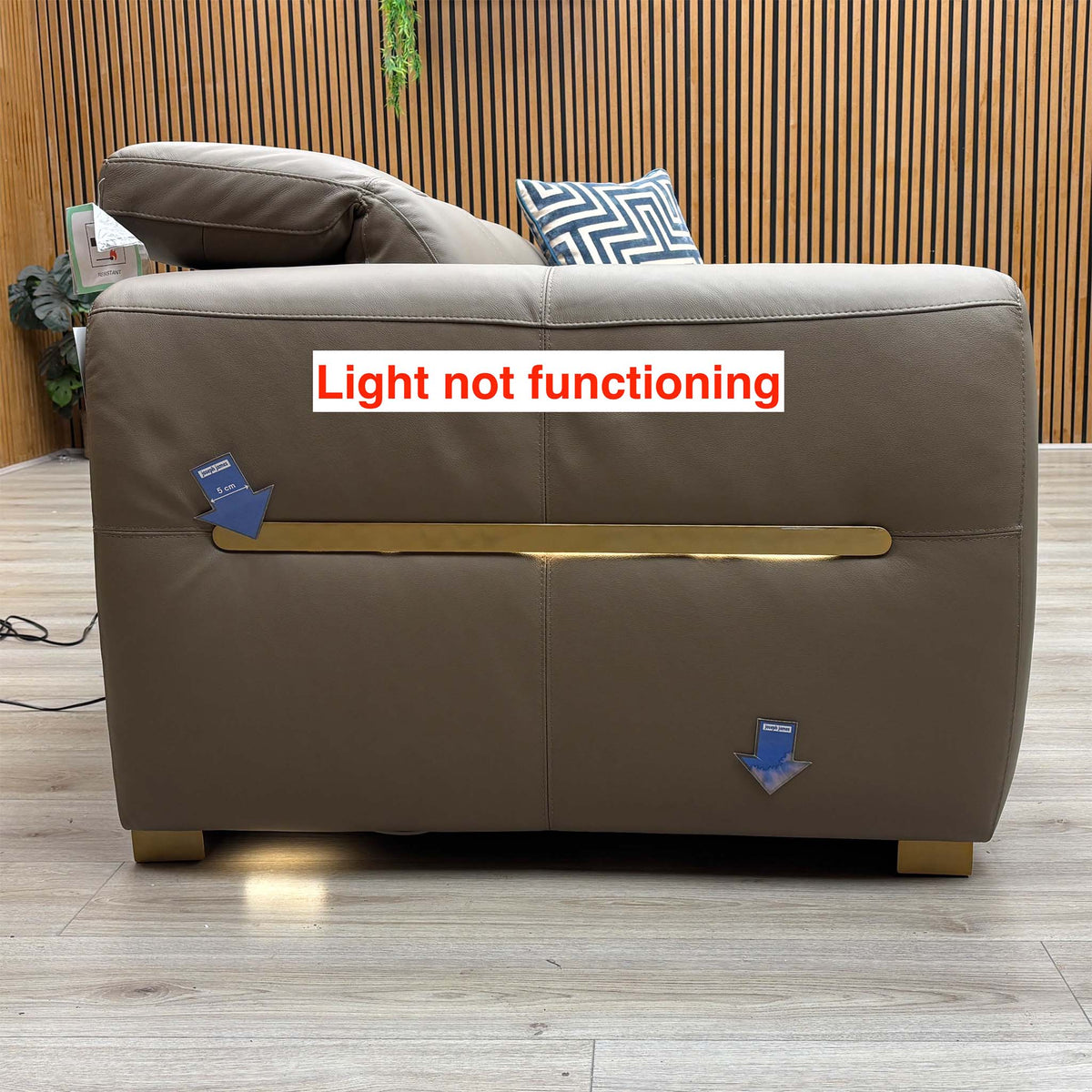 Back of the Edison taupe leather sofa with the light strip marked as not functioning, arrows on the back panel