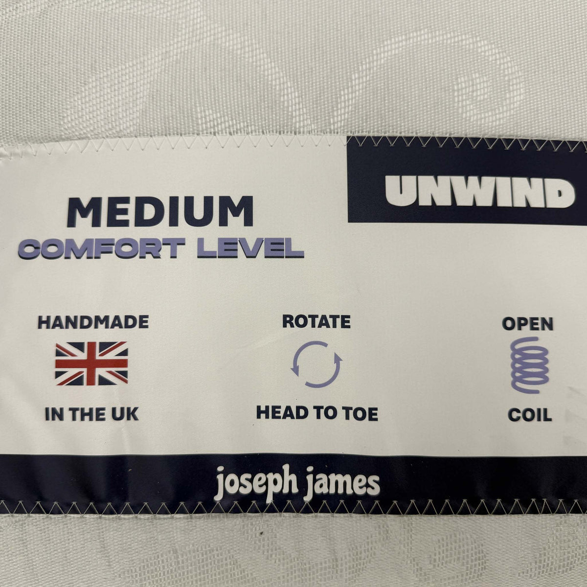 Unwind mattress label on the Gus guest bed showing medium comfort level, open coil, handmade in the UK