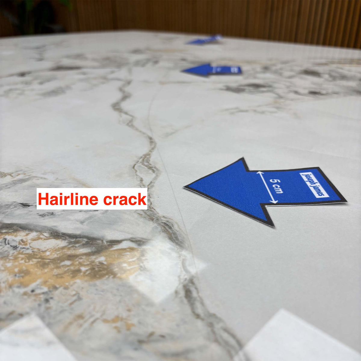 Close-up of a third hairline crack running along the Avorio ceramic table top, blue 5cm arrow for scale
