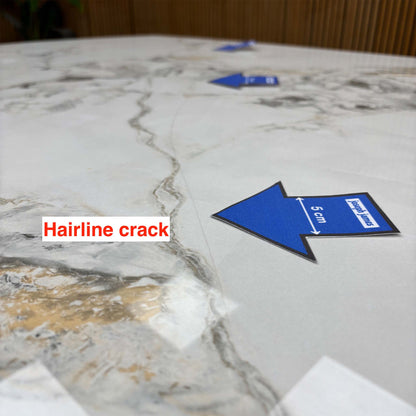 Close-up of a third hairline crack running along the Avorio ceramic table top, blue 5cm arrow for scale