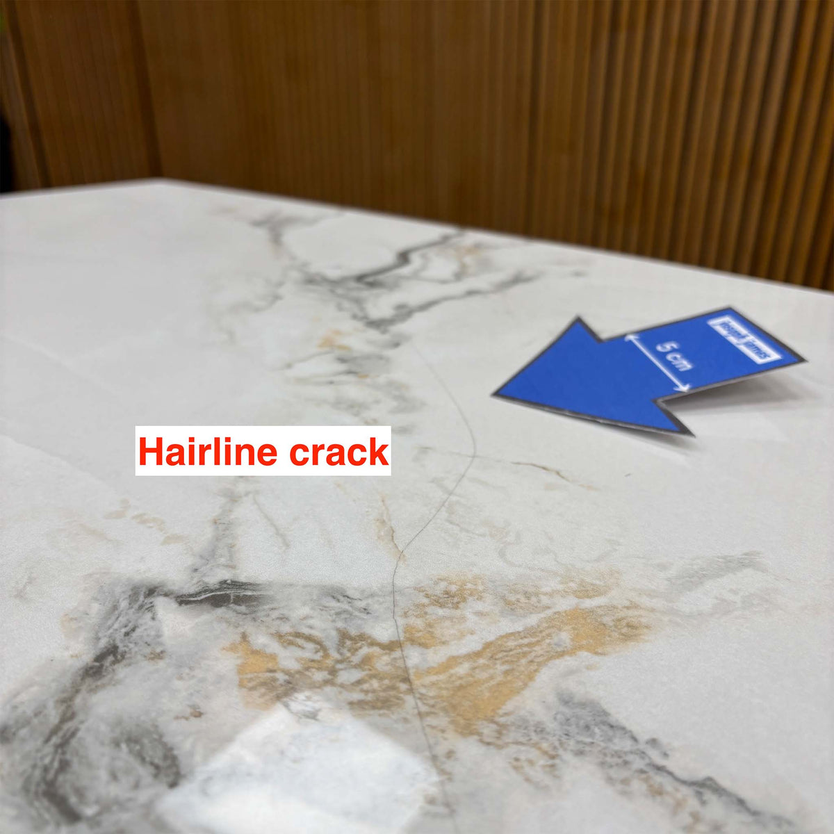 Close-up of a hairline crack on the Avorio ceramic table top, marked with a blue 5cm arrow