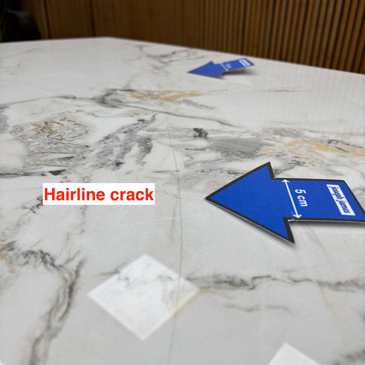 Close-up of a second hairline crack on the Avorio ceramic table top near the grey veining, blue 5cm arrow