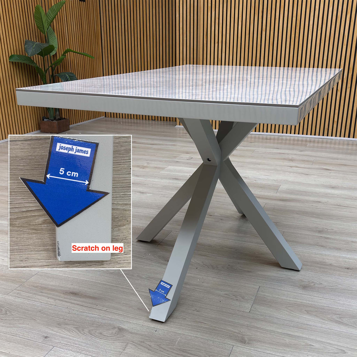 Fumo grey dining table with a scratch on one leg near the foot, marked with a 5cm arrow sticker and shown in an inset