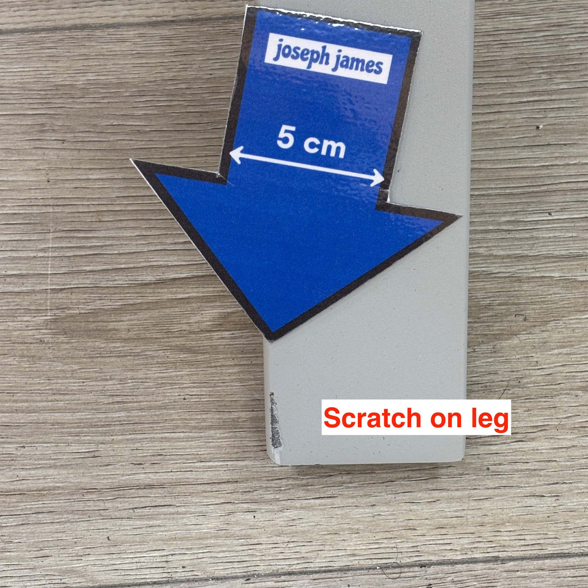 Close-up of the scratch on the grey metal leg of the Fumo dining table, with a 5cm arrow sticker for scale