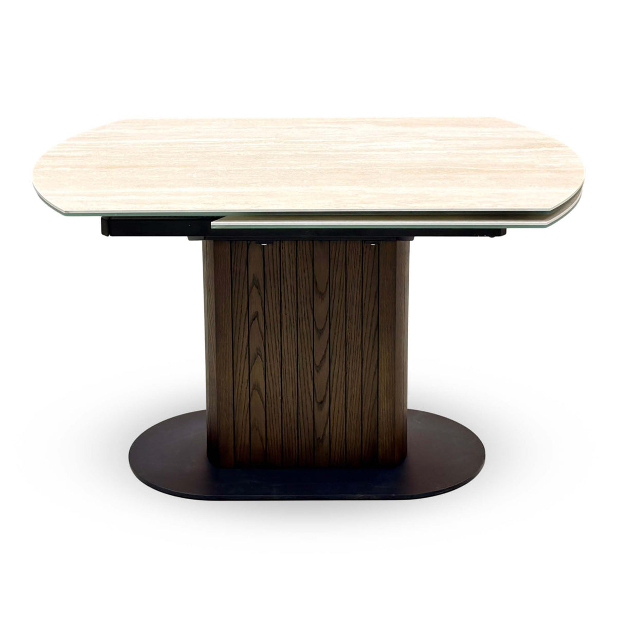 Front view of the Tiber travertine ceramic table closed, dark wood ribbed pedestal on an oval base