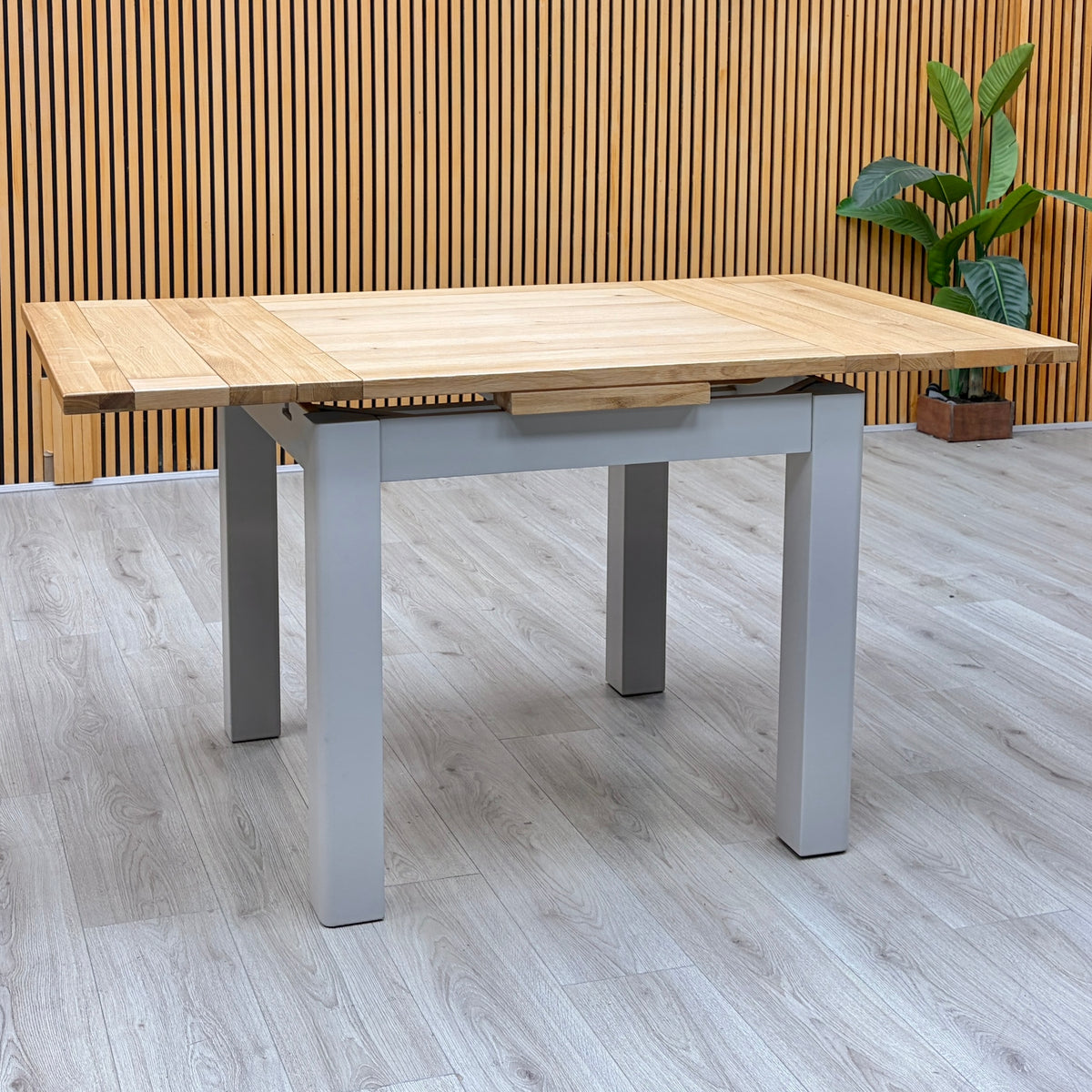 Lewis solid oak small draw leaf extending dining table, fully extended with grey painted legs in the showroom