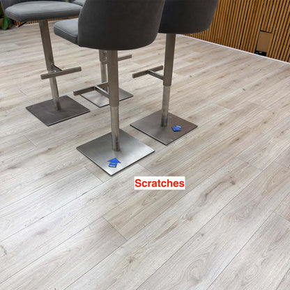 Grigio grey fabric bar stools on an oak floor with scratches on two steel bases marked by blue arrows