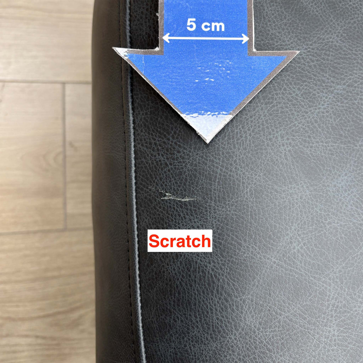 Close-up of a small scratch on the side of the Romilly navy leather footstool, marked with a 5cm arrow