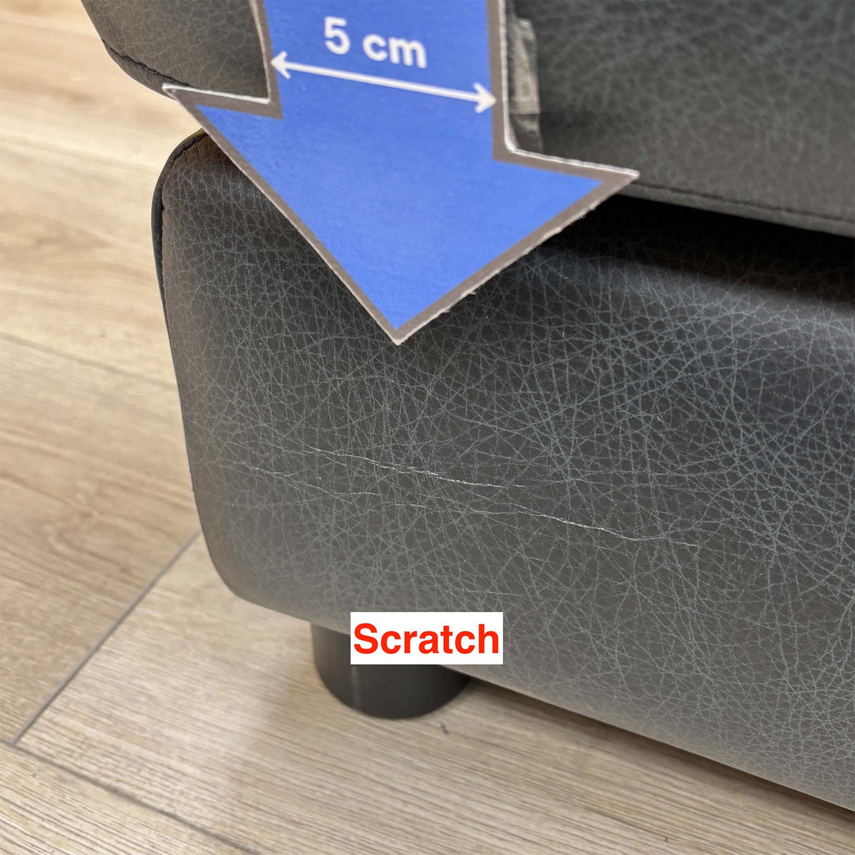 Close-up of a scratch on the base of the Romilly navy leather footstool near a foot, 5cm arrow for scale