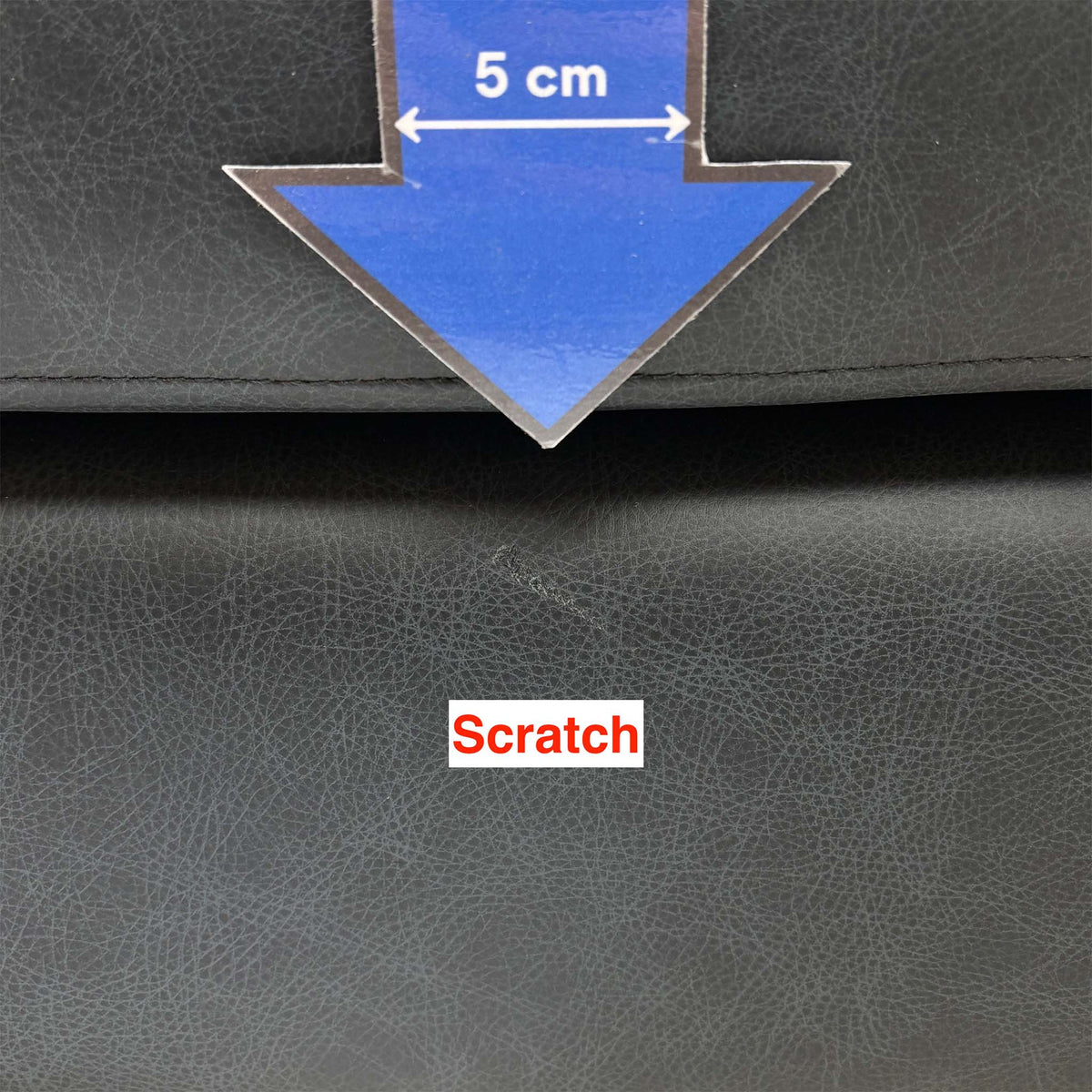 Close-up of a faint scratch below the top seam of the Romilly navy leather footstool, 5cm arrow for scale