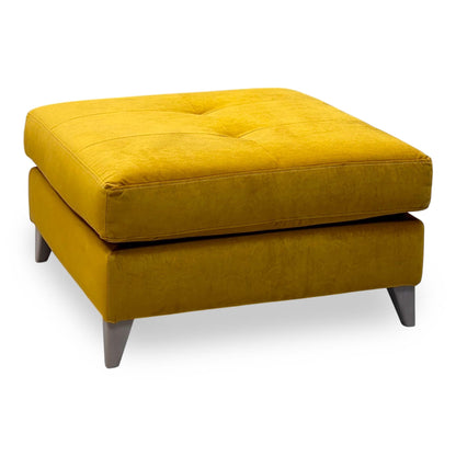 The Lounge Co. Hermione amber yellow velvet footstool with a buttoned top and grey tapered legs, angled view from the left