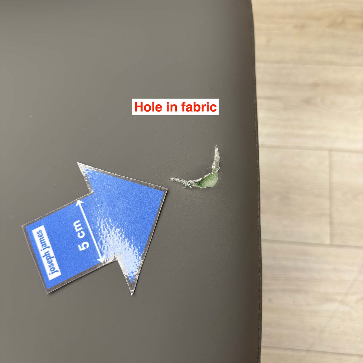 Close-up of the hole in the faux leather on a Quattro stone grey swivel chair seat, 5cm arrow marker for scale