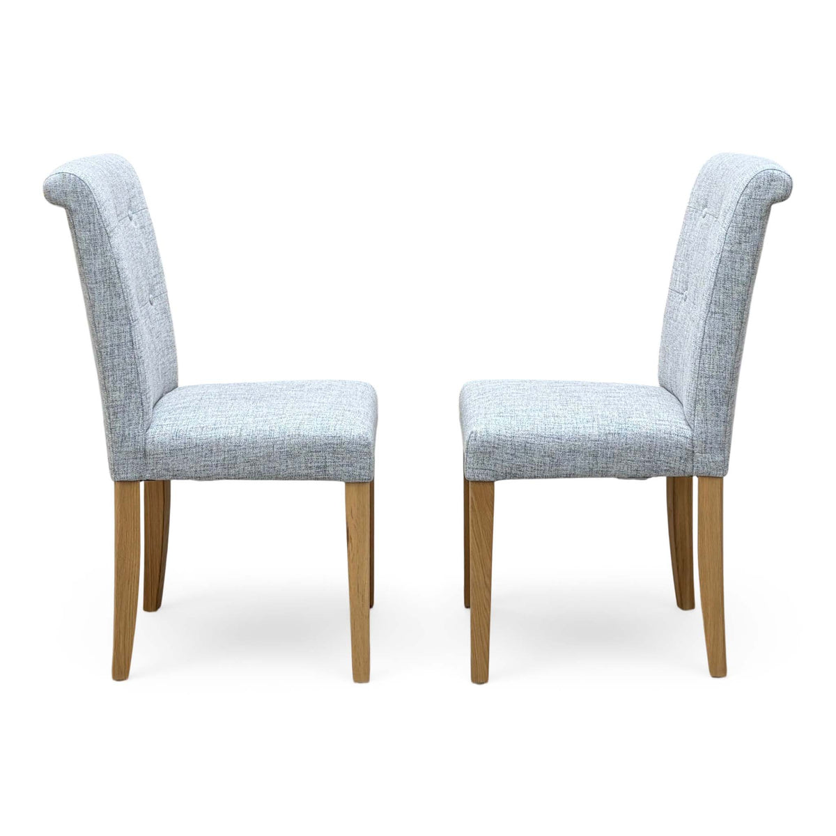 Side angle of the Augusta mist grey fabric pair of roll back dining chairs showing the scroll top and oak legs