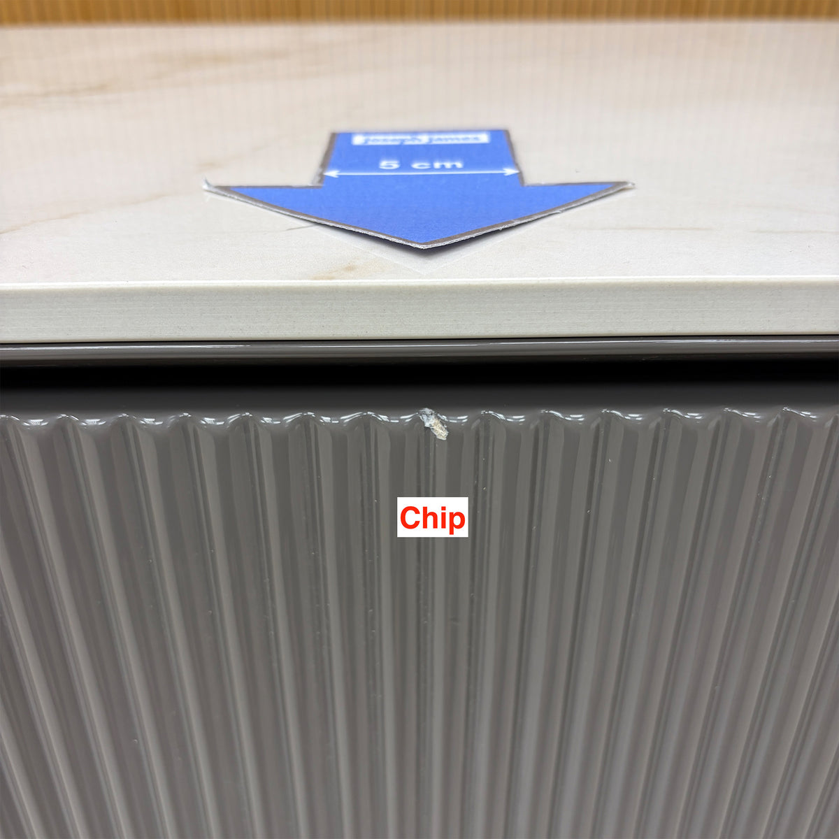 Close-up of a small chip on the top edge of a fluted door on the Ivy grey sideboard, 5cm arrow for scale