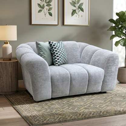 Rhianna lead grey fabric cuddler chair in a living room with a table lamp, patterned rug and fig plant