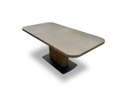 Close-up detail of the Jai dining table's pedestal base, featuring vertical linear grooves and a square black metal plinth at the bottom.