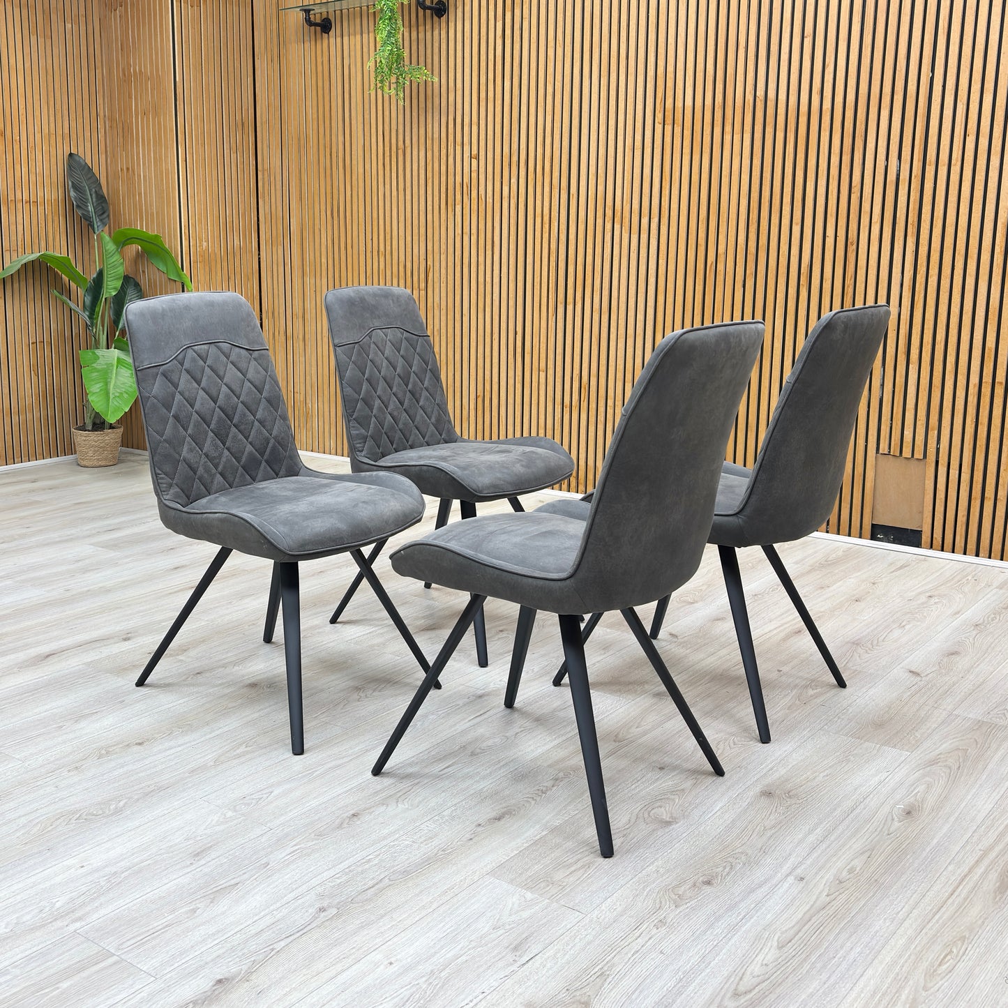 Angle view of the Warrior grey dining chairs arranged in a modern dining room setting, showcasing their quilted backrest design.