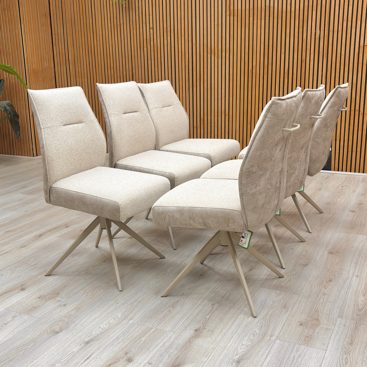 Six Mirage neutral fabric swivel dining chairs in two rows against a slatted wood wall