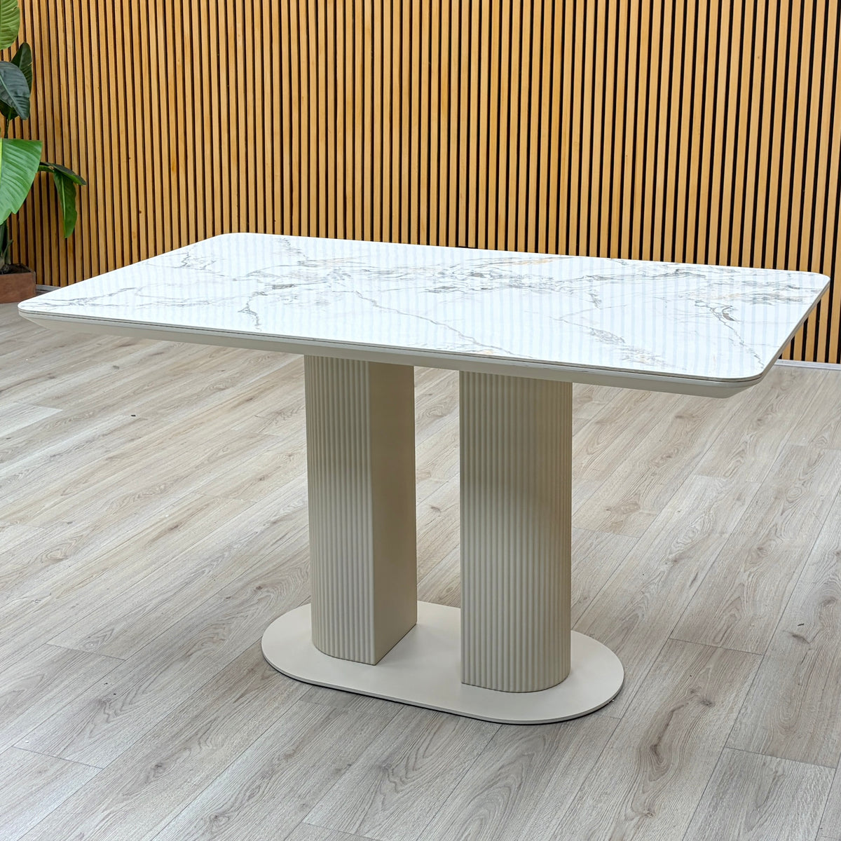 Avorio white marble effect ceramic top fixed dining table photographed against a slatted wooden wall