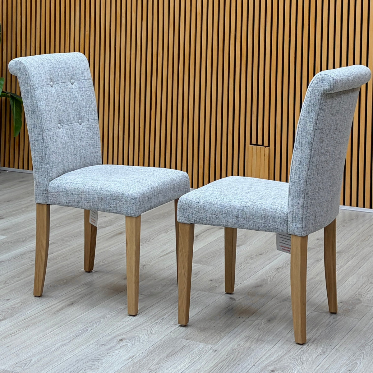 Augusta mist grey fabric pair of roll back upholstered dining chairs photographed against a slatted wooden wall