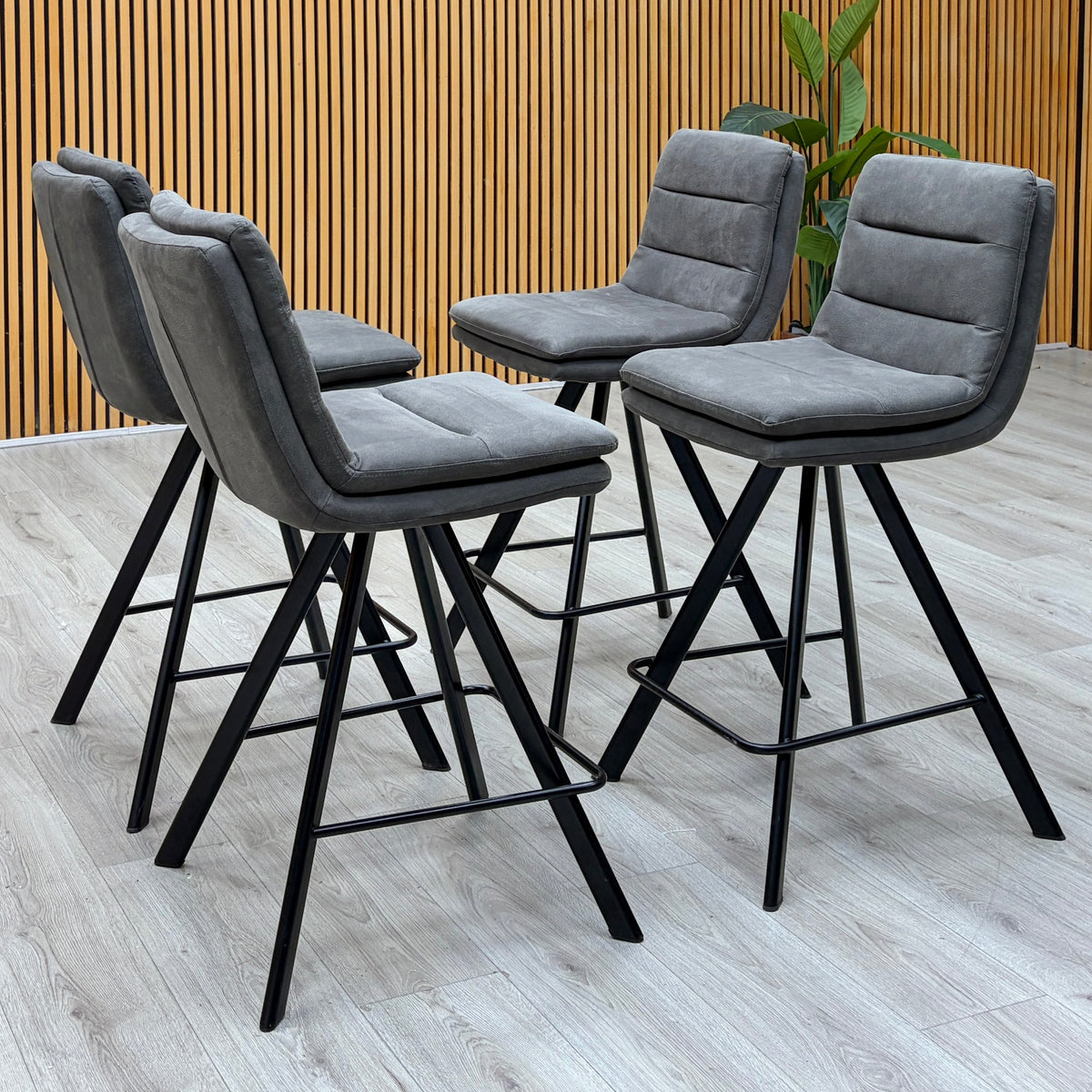 Bodahl Njord anthracite grey fabric set of 4 bar stools against a slatted wooden wall on a light oak floor