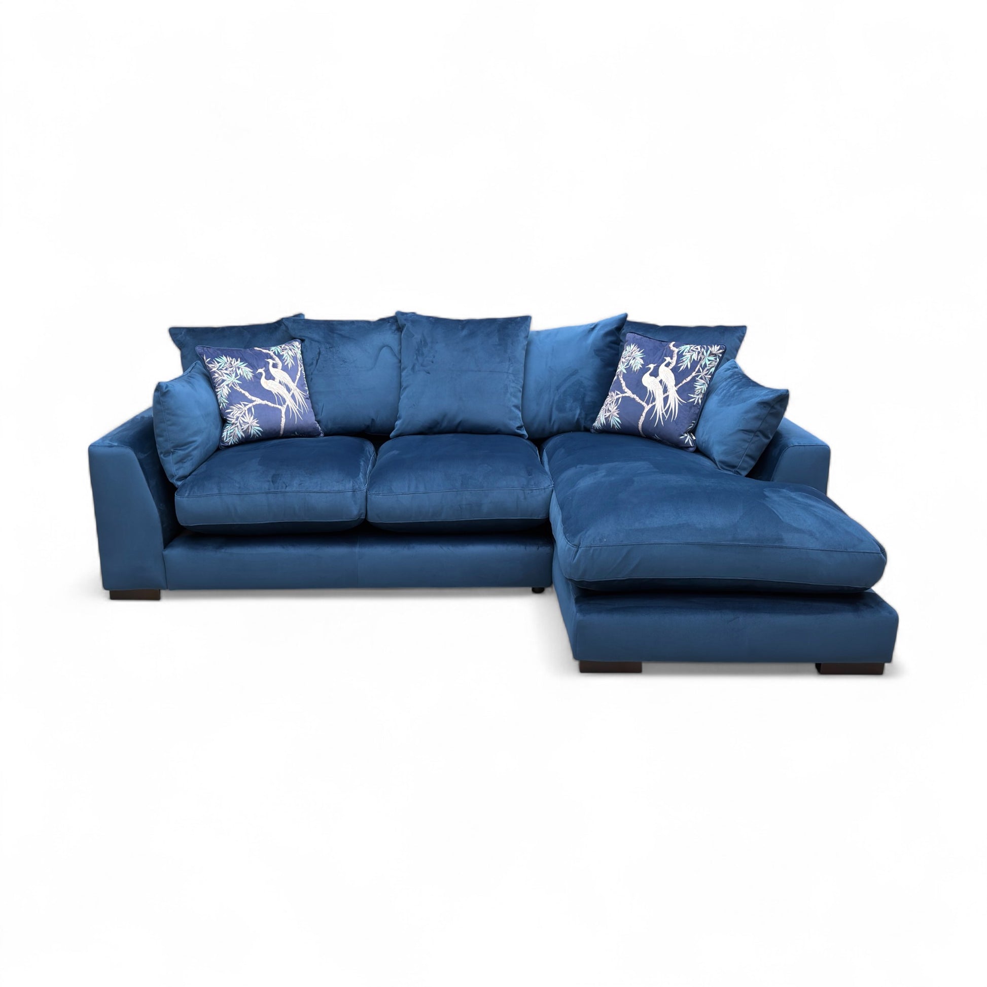 Frontal view of the ‘Plush’ chaise sofa, emphasizing the deep blue velvet fabric and the relaxed, inviting look of the pillow cushions.