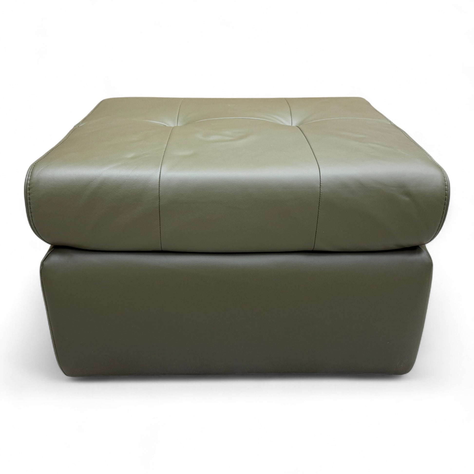 The 'Ava' khaki green leather footstool positioned in a living space, demonstrating its use as an ottoman or extra seating.